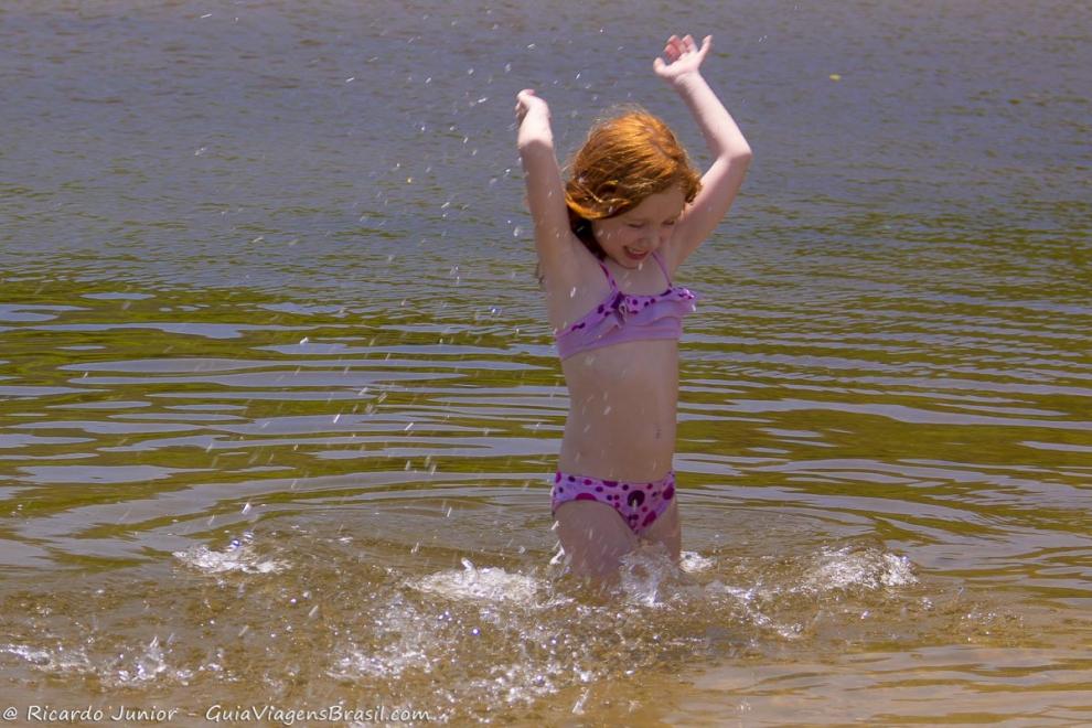 Imagem de uma menina jogando água pra cima na piscina natural.